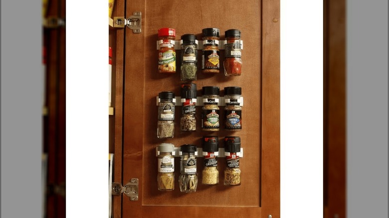 12 plastic seasoning containers hanging onto a cabinet door via the Bellemain Spice Gripper Clip Strips from Target on a white background.