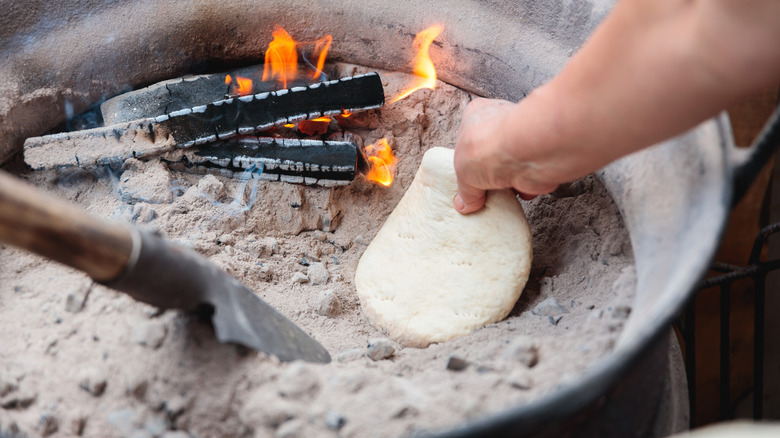 A person places dough straight onto ashes to cook