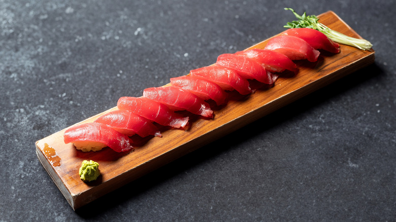 Slices of lean red tuna on a wooden serving tray with fresh herbs and wasabi