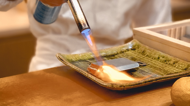 Sushi chef using a torch to sear a piece of tuna