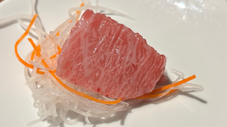 Close up picture of a slice of kamatoro on a bed of noodles on a white plate