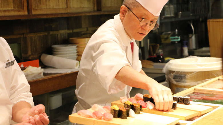 A chef arranging pieces of sushi on a wooden board