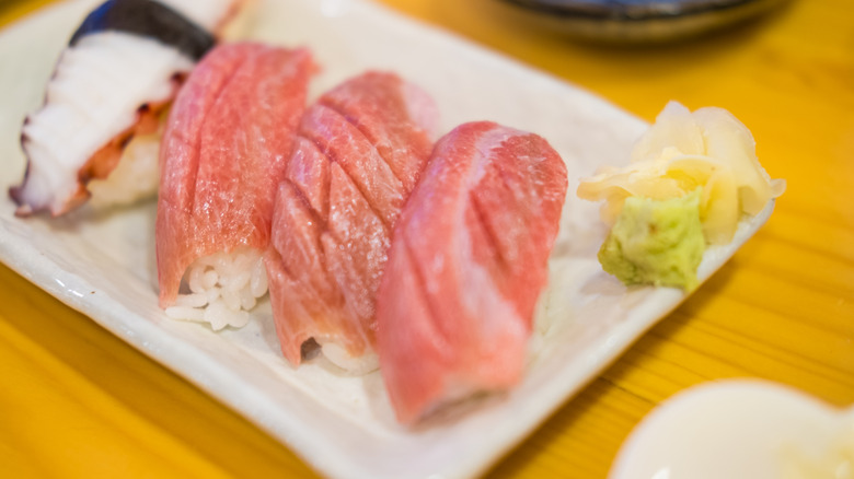 Light pink, fatty tuna on a rectangular white plate with fresh ginger and wasabi