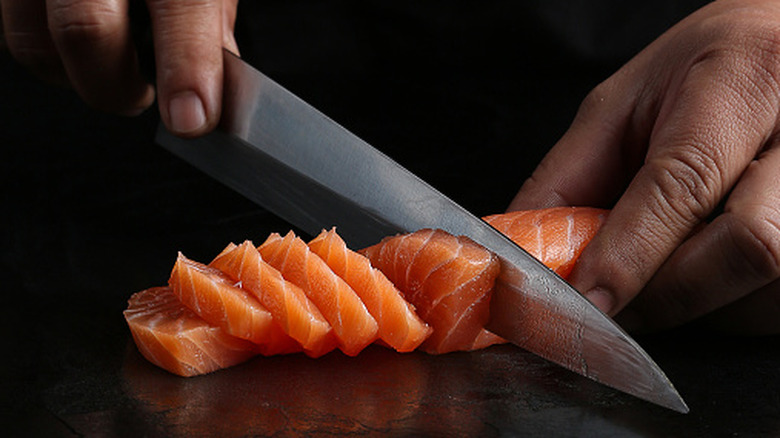 Chef's hands slicing thin pieces of sashimi with a sharp knife