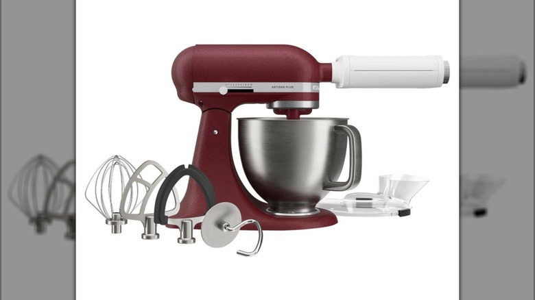 A red KitchenAid stand mixer with an attached pasta maker plus various other tools beside it on a white background.