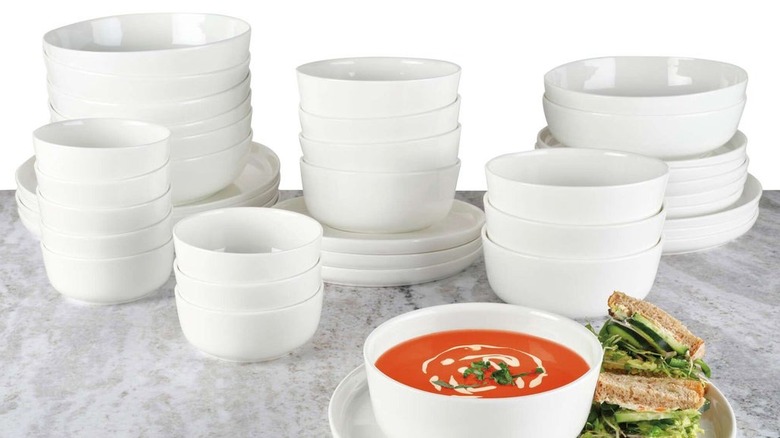 A set of white plates and bowls on a grey surface with one bowl and plate in the front holding soup and a sandwich