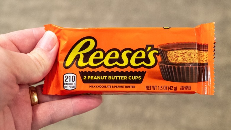 A hand holding a package of Reese's Peanut Butter Cups.