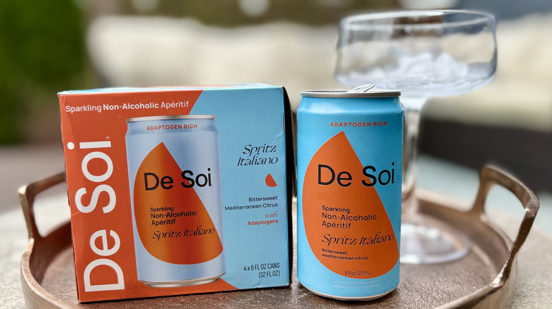 A box and can of De Soi Spritz Italiano on a tray with a coupe glass
