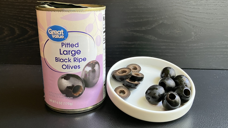 A can of Great Value pitted large black ripe olives and a white dish displaying both whole and sliced olives