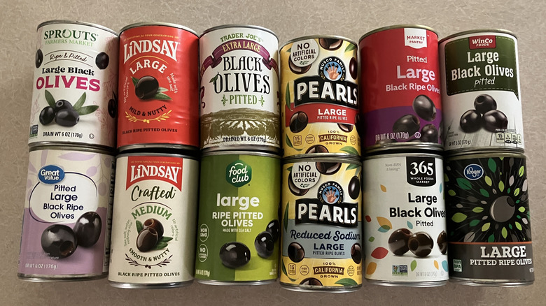 Twelve cans of black olives from different brands in two rows