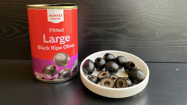 A can of Market Pantry pitted large black ripe olives and a white dish displaying both whole and sliced olives
