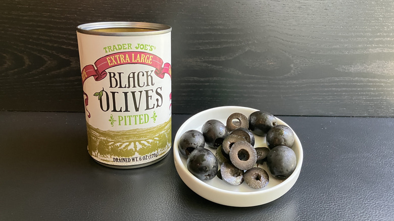 A can of Trader Joe's pitted black olives and a white dish displaying both whole and sliced olives
