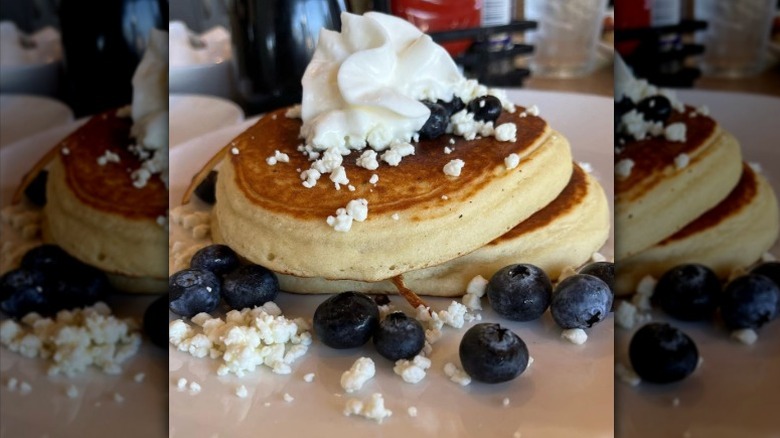Two pancakes topped with blueberries, goat cheese, and whipped cream on a plate