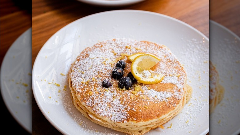 Two pancakes with blueberries, lemon zest, and a lemon slice on top