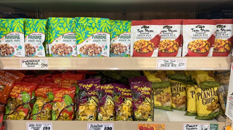 Various salty snacks on Trader Joe's grocery shelves, including plantain chips and furikake snack mix