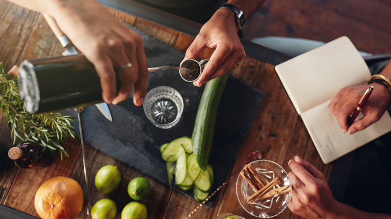 Top view of man pouring mixture into a jigger to prepare a cocktail and another taking down notes.