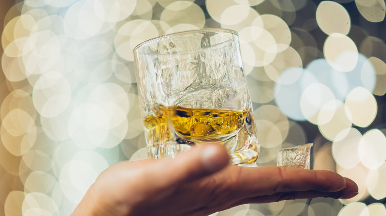 Hand holding glass of whiskey on candle or light bokeh background