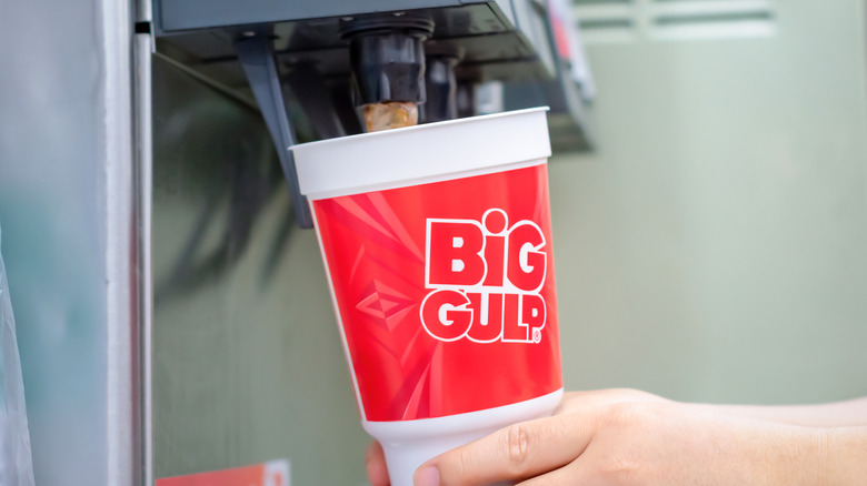 Hands holding a Big Gulp cup under a soda machine