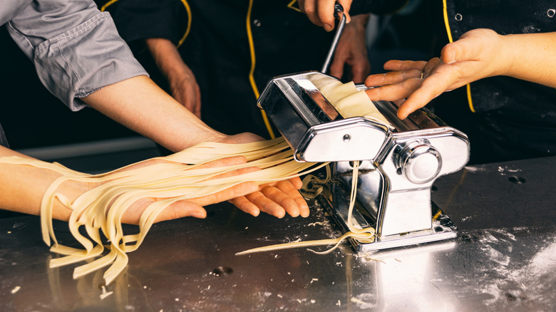 Two people making ribbons of pasta in a pasta machine