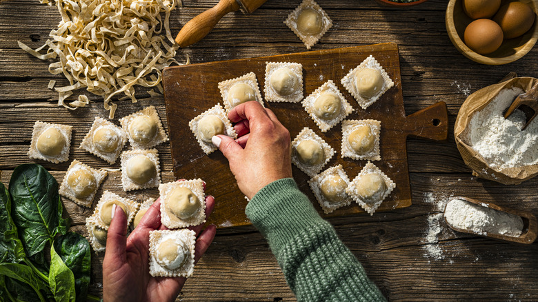 Woman in green sweater picking up fresh ravioli from a table