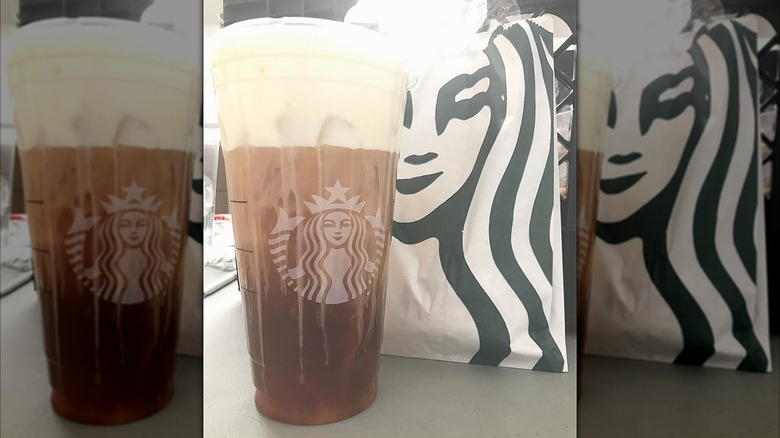 An iced tea drink topped with cold foam in a clear Starbucks cup