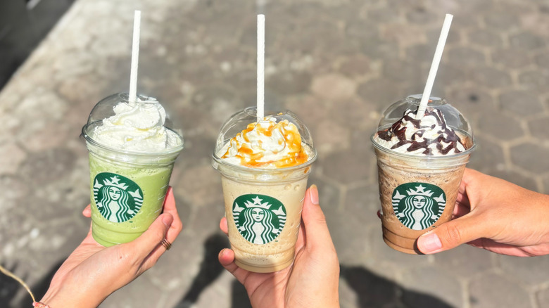 Three hands, each holding a colorful blended Starbucks drink