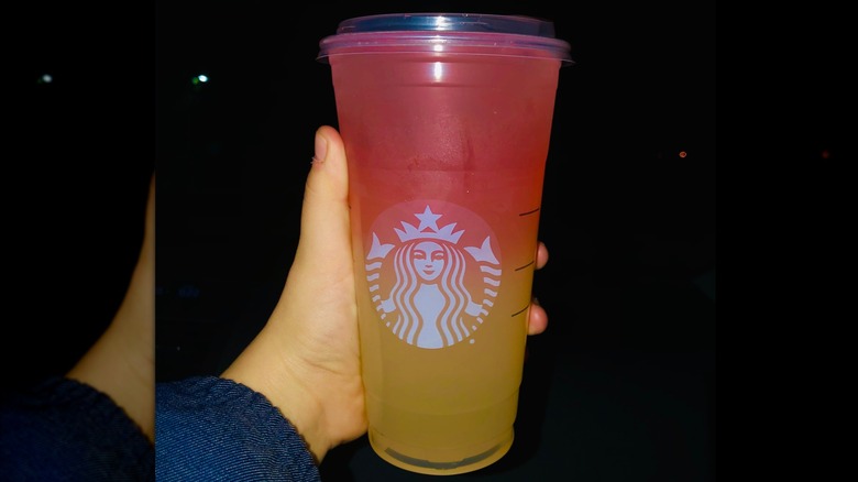 Hand holding a pink and yellow Starbucks lemonade drink