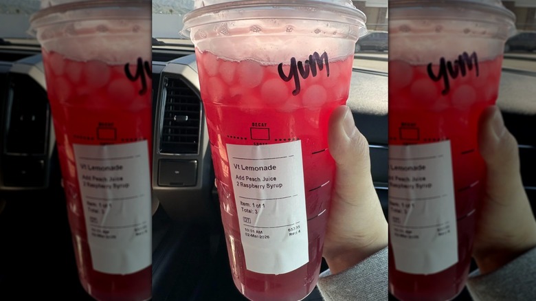 A large red ice drink in a plastic cup being held by a hand