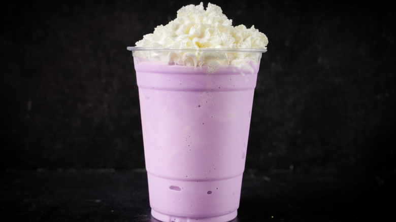 A pinkish purple Frappucino topped with whipped cream on a black background