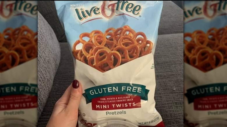 A hand holding a bag of liveGfree gluten free pretzels above a grey sofa