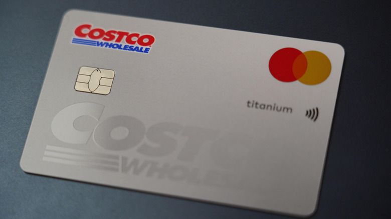 A close-up shot captures a silver Costco Wholesale Mastercard titanium credit card resting on a dark surface, highlighting its EMV chip, contactless payment symbol, and brand logos.