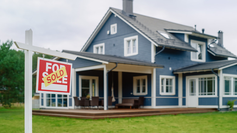 Red Property Sold Sign in a Garden in Front of a Big Blue Stylish House with Traditional Architecture.