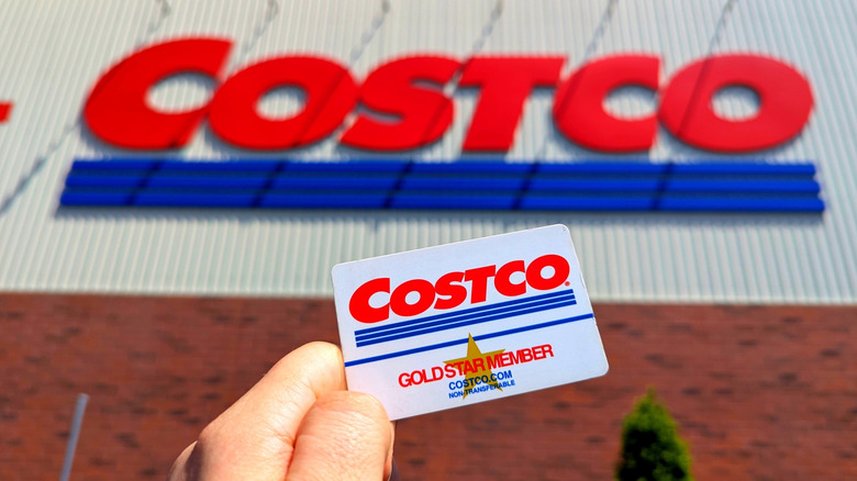 Costco Wholesale Gold Star Membership Card Held In Hand in Front of Storefront Location.