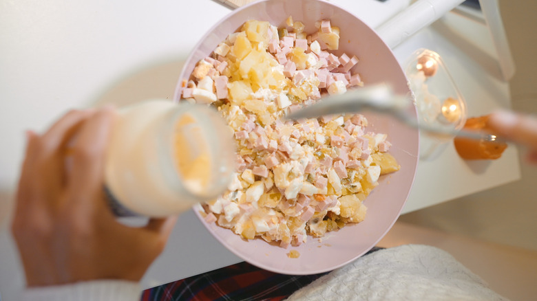 Potato salad being mixed with mayonnaise in a bowl