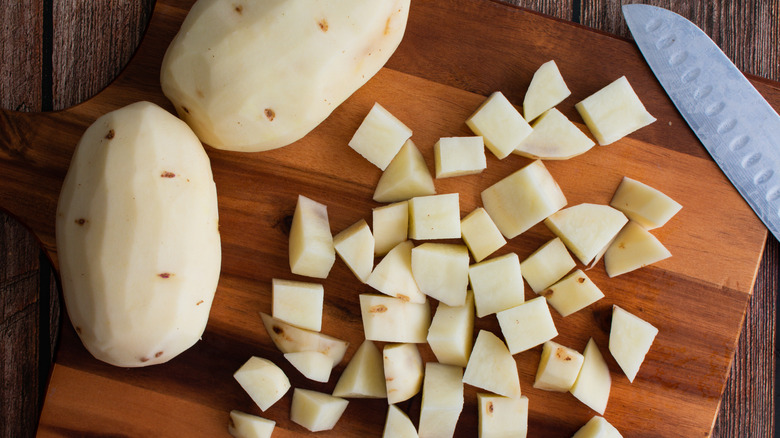 Fresh potatoes chopped into small cubes with a kitchen knife and chopping board