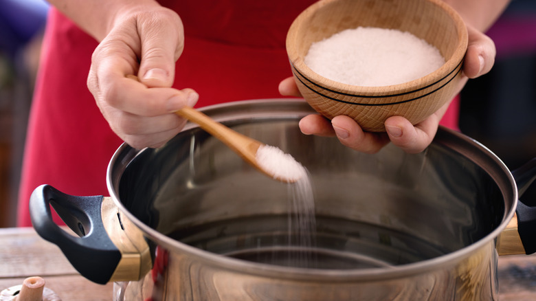 Hands holding a wooden bowl with salt, seasoning a pot of water