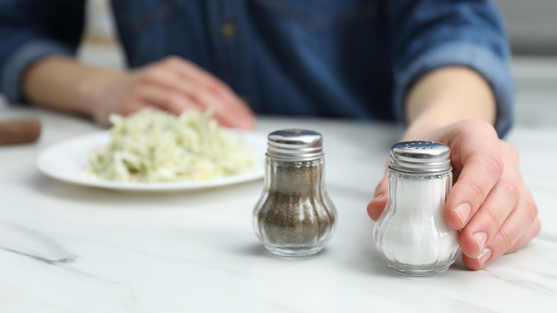 Person's hands holding salt and pepper shakers at a dining table