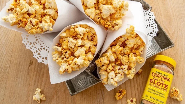 Shaker of Everything But The Elote Seasoning Blend alongside cones of seasoned popcorn