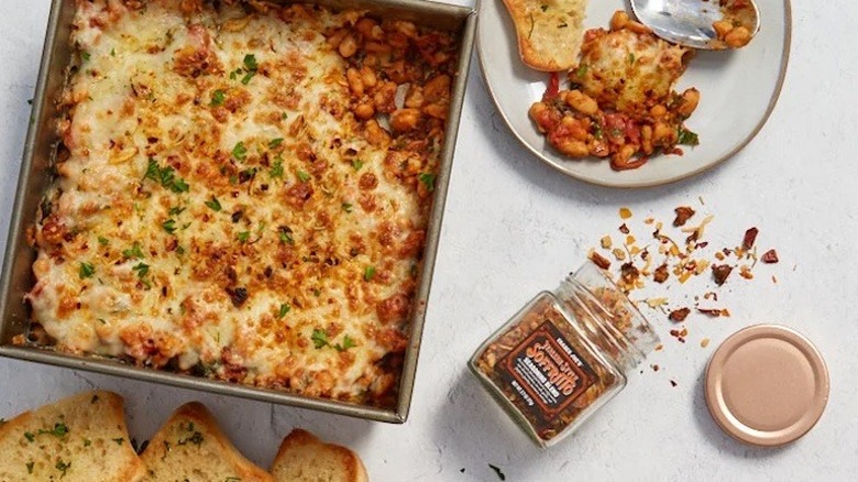 Open jar of Trader Joe's Italian Style Soffritto Seasoning Blend alongside pan of cheesy baked beans
