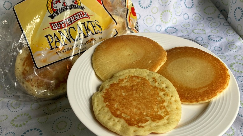 A plate with three cooked pancakes next to a clear bag of frozen pancakes from De Wafelbakkers brand