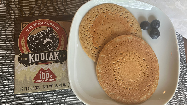 A plate with two pancakes and some blueberries set atop a box of Kodiak Flapjacks