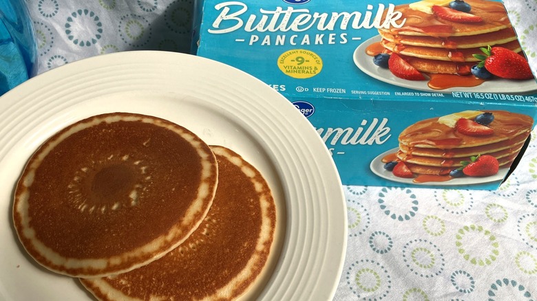 A plate with two decorative pancakes and a blue box of frozen pancakes