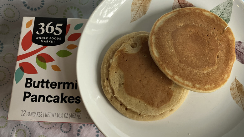 A plate with two pancakes set atop a box of 365 Whole Foods Market Buttermilk Pancakes