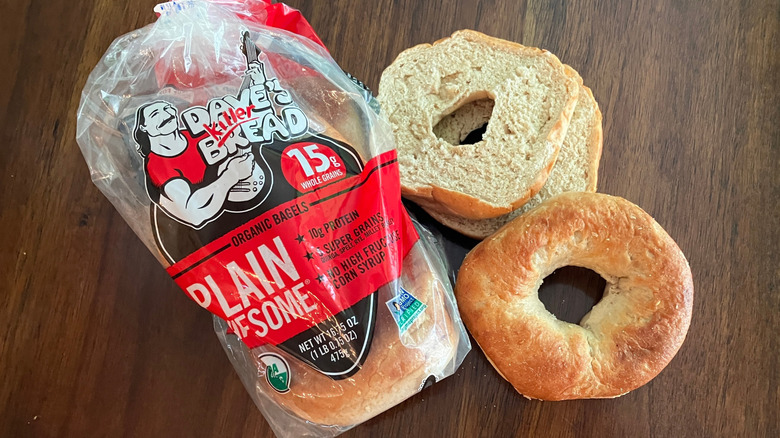 Bagels stacked on a wooden table next to a bag of Dave's Killer Bread bagels.