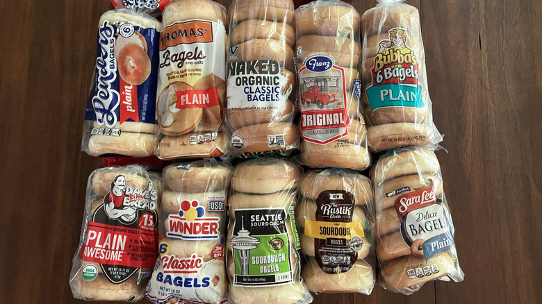 Ten plastic sleeves of name brand grocery store bagels on table, including brands like Sara Lee, Wonder, and Rustik