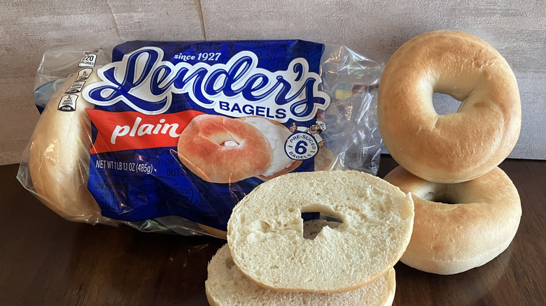 Bagels displayed beside a bag of Lender's bagels on table.
