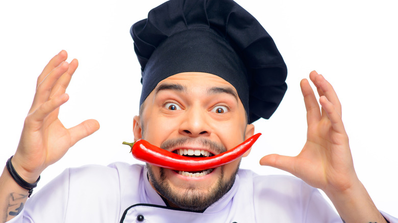 Chef in black hat with red chili pepper in his mouth and hands up