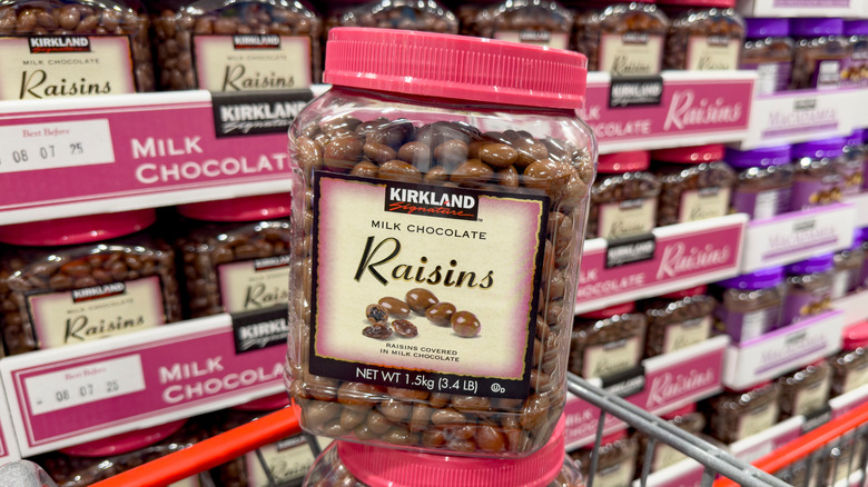 Large jar of Kirkland Signature milk chocolate raisins stacked on top of another in cart with other containers in the background