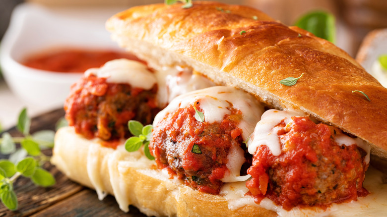 Meatball sandwich holding three meatballs with sauce and cheese on them.