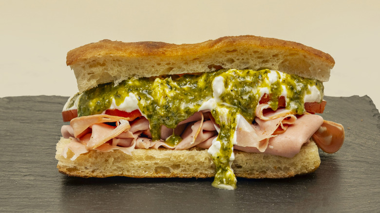 Focaccia sandwich with mortadella, sliced tomatoes, creamy cheese, and pesto